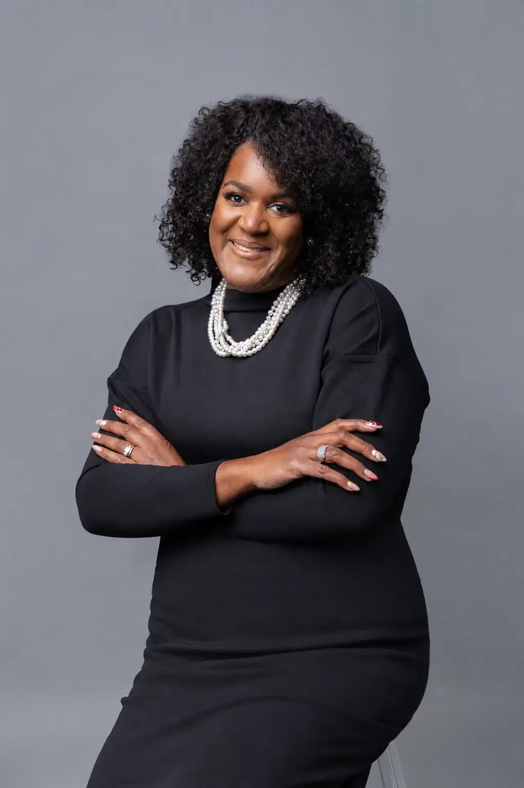 Dr. Keisha Scarlett in a black studio portrait, arms folded and looking toward the camera