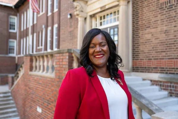 Dr. Keisha Scarlett in a red blazer outside a brick civic building